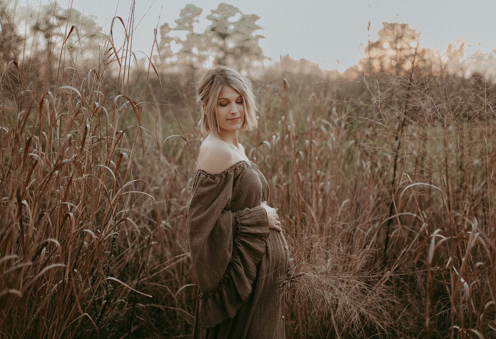 Beautiful pregnant woman in a romantic maxi dress posing amidst high grass during her sunset maternity session near Durham Women's Clinic. The portrait was taken by Raleigh maternity photographer - Victoria Vasilyeva Photography.