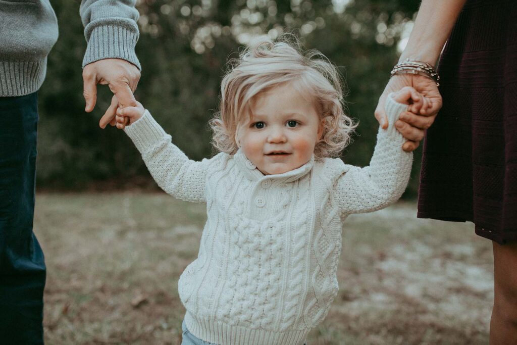 Blonde hair toddler holds mom and dad and looks straight at the camera. The portrait was taken near Durham pediatric office by Victoria Vasileva Photography.