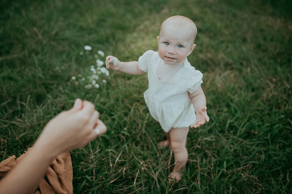 1 year-old girl in wite boho romper among high grass