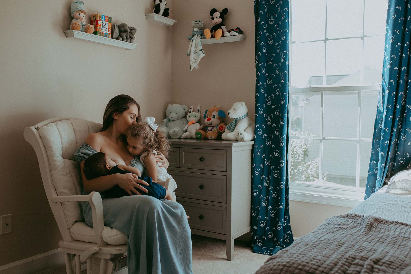 mom in blue maxi dress breastfeed her baby boy and hud older sibling in nursery room raleigh nc