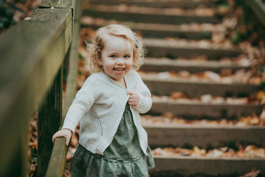 baby girl wears white knitted jumper and green dress staying on a stair in raleigh nc park
