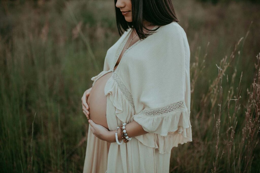 pregnant woman in ivory maternity robe holds belly and looks down during maternity session with victoria vasilyeva photography