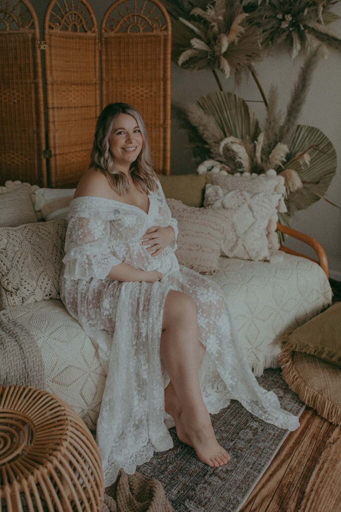 pregnant woman is sitting on a sofa at boho styled photography studio near doula raleigh nc