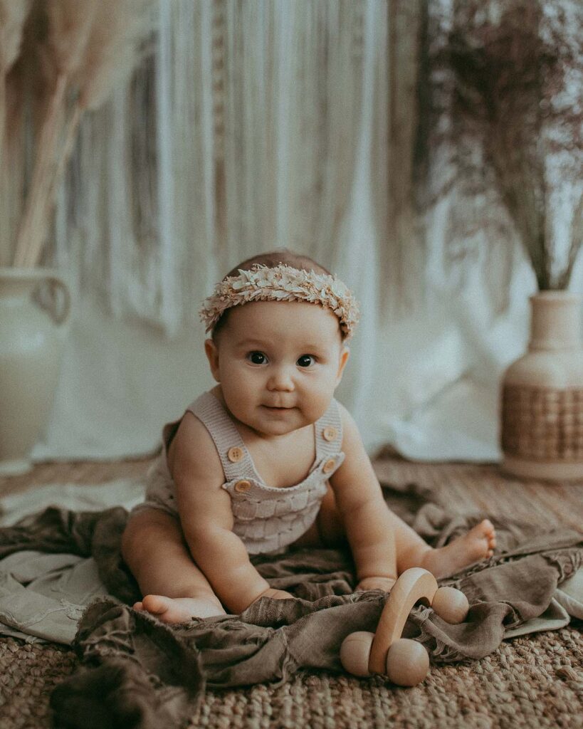 Baby girl is sitting on a jute rug and looking at camera during portrait session with Apex baby photographer near Triangle Mothercare Doula and Night Nurse Agency