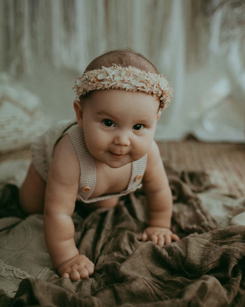 adorable baby girl in boho flower halo and tan knitted romper is crawling to the camera during baby photo session with Victoria Vasilyeva Photography.