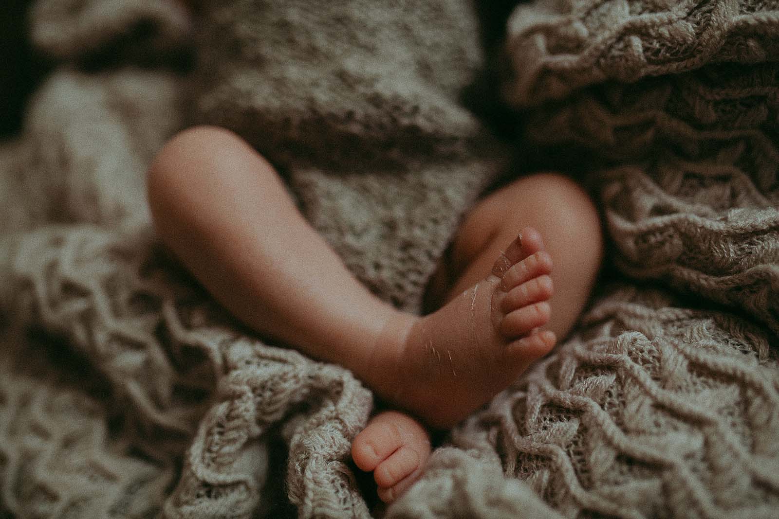 Criss-cross newborn baby's legs with flaky skin swaddled in cozy knitted grey blanket. Baby photo session took place at Victoria Vasilyeva Photography Studio in Apex NC