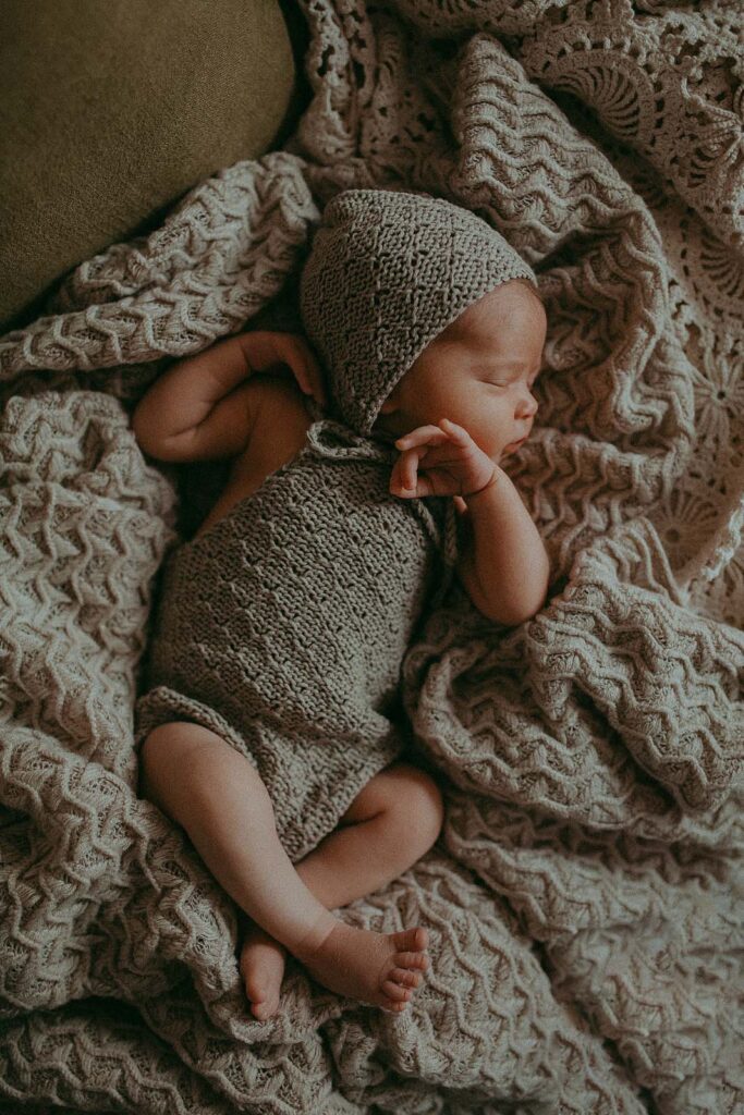 Tiny girl in grey knitted romper and hat is sleeping on a couch during her first ever photo session with Apex newborn photographer.