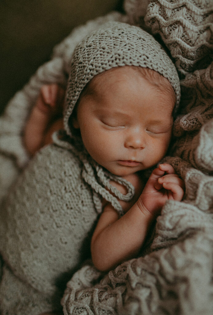 Newborn baby girl in knitted grey hat and romper is sleeping during photography session at Apex photo studio