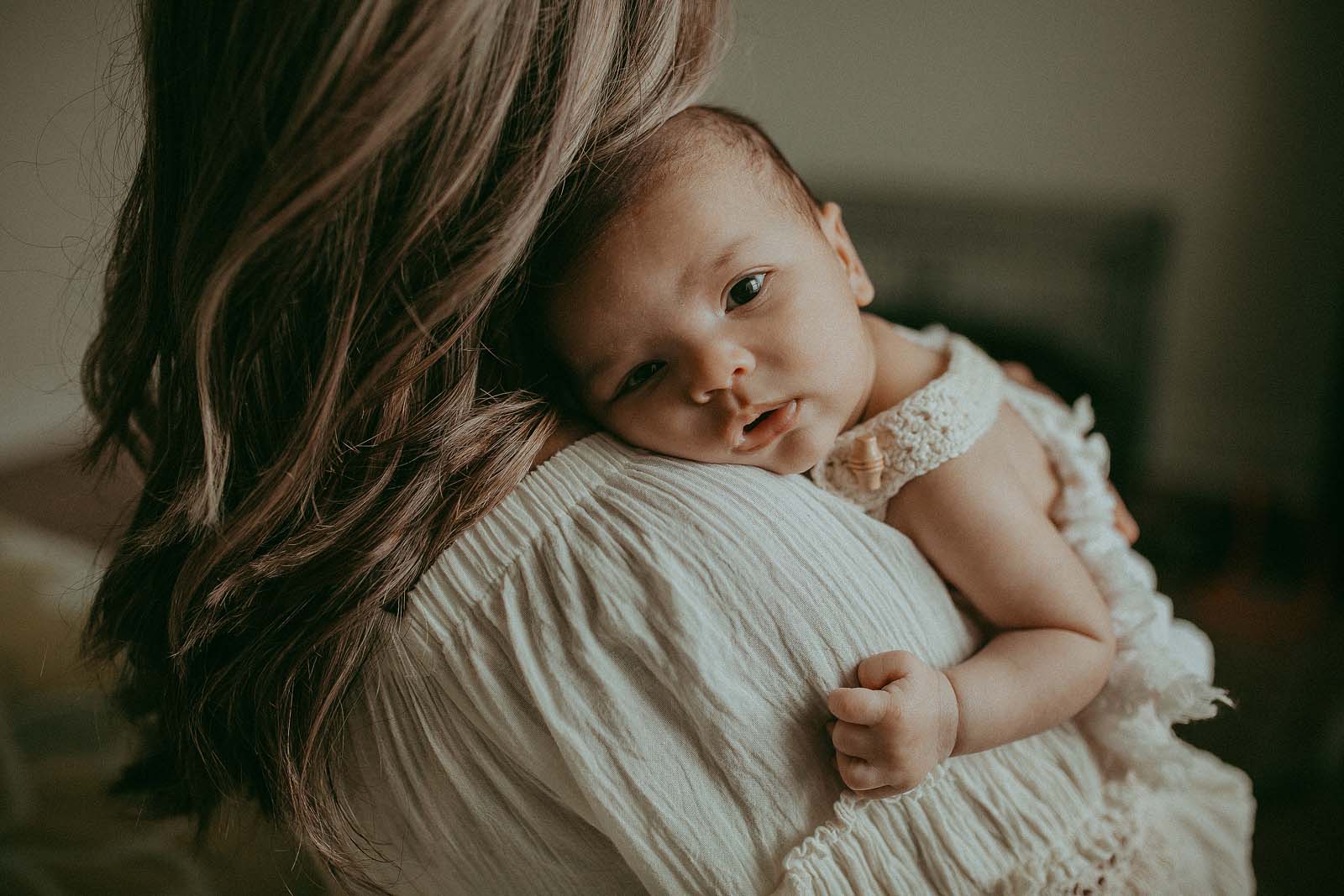 Mom with long dark hair hugs her newborn baby boy. He has big brown eyes and dark hair. The portrait was made by Victoria Vasilyeva Photography - Raleigh Family Photographer.