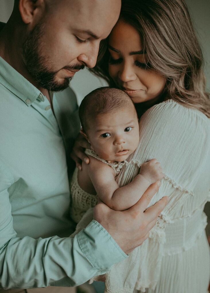 Mom in off-white maxi boho dress and dad hold thier baby boy who is looking at the camera during thier family photo session with Victoria Vasilyeva Photography - Raleigh Family Photographer.