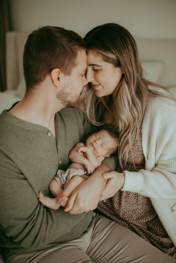 The beautiful couple just welcomed their baby boy. They are full of love and tenderness. They hold him and lean their faces to each other. This portrait was taken during the newborn photo session with Victoria Vasilyeva Photography
