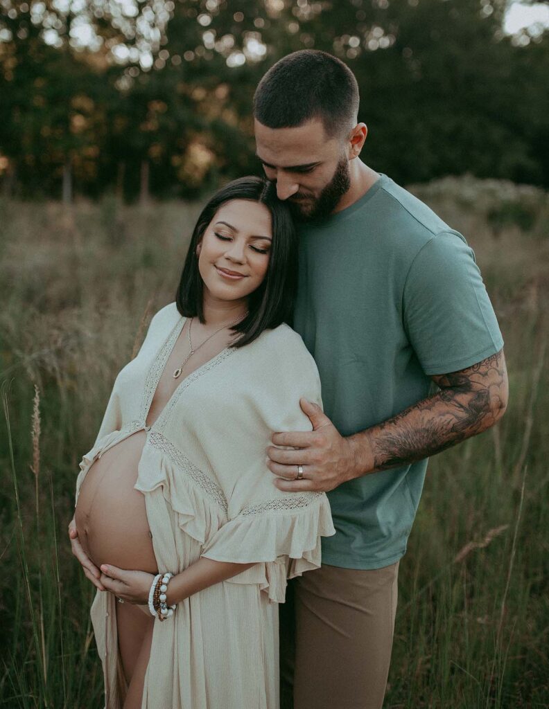 A stunning maternity photo by Victoria Vasilyeva Photography showcases an expecting mother in a graceful boho maxi dress, lovingly supported by her partner, reflecting the serenity and bliss they experienced after their visit to a prenatal massage Fayetteville NC.