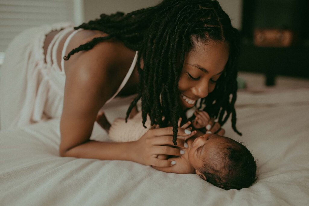 A beautiful family moment unfolds at home as mom with long black hair in her stunning off-white maxi dress hugs her 9-day-old baby boy. Photo session took place in Raleigh NC.