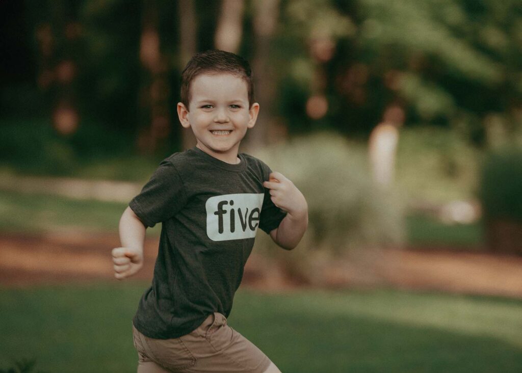 A family photographer captures a special moment of 5 years old boy. He is smiling and running around. The portrait by Raleigh family photographer - Victoria Vasilyeva Photography near North Raleigh Pediatricians.