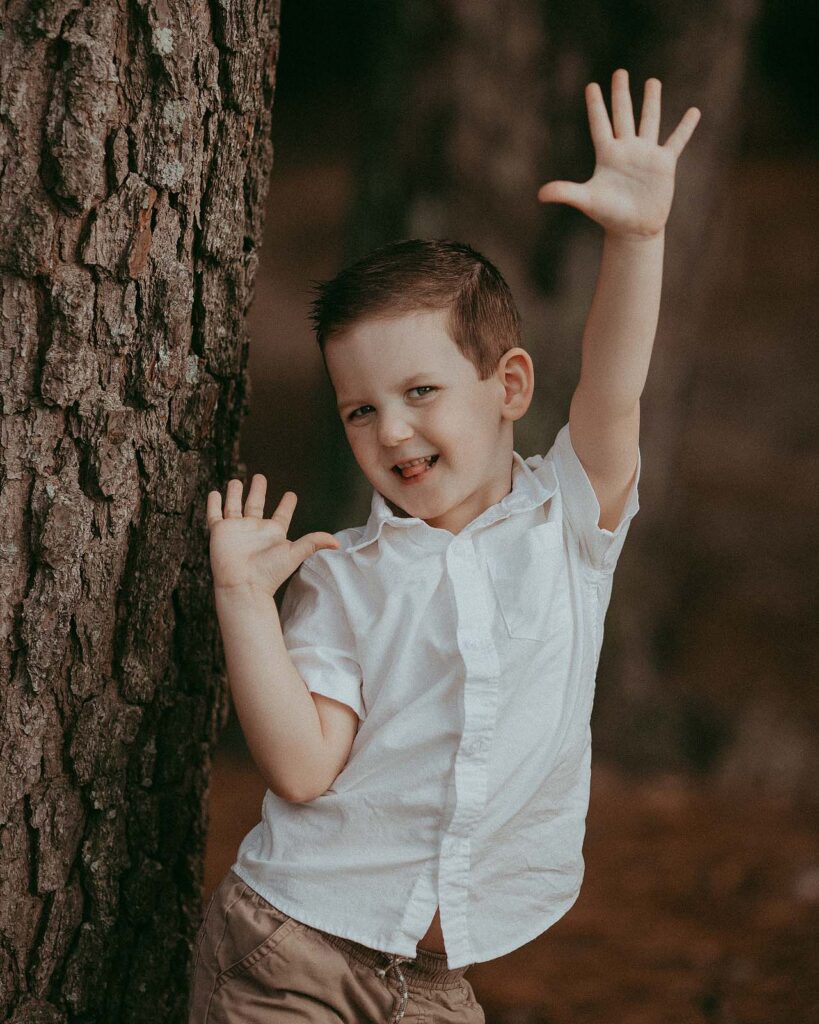Cute and funny 5 years old boy in white shirt shows his tounge, smile and makes silly faces during his 5th birthday photo session with Raleigh family photographer near North Raleigh pediatricians.