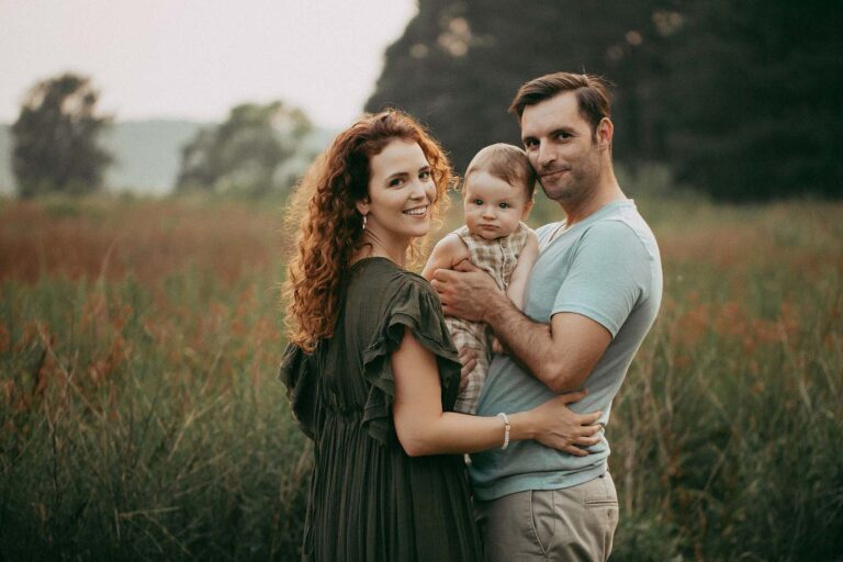 A family of three poses near A Woman's Place in Fayetteville, NC. The mother has long red curly hair and wears a maxi boho dress. The father has short dark hair and beautiful eyes. The baby boy is 8 months old and has huge blue eyes.