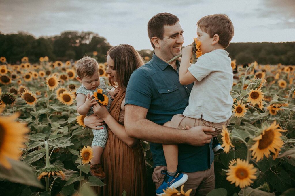 Family of four pose to Raleigh family photographer at Sunflower Field Dorothea Dix Park.