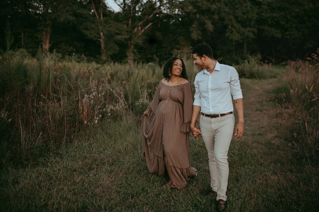 Expecting couple holds the hands and walks together down the path. Maternity photo session took place near Baby Shower Venues Cary NC by Victoria Vasilyeva Photograher.