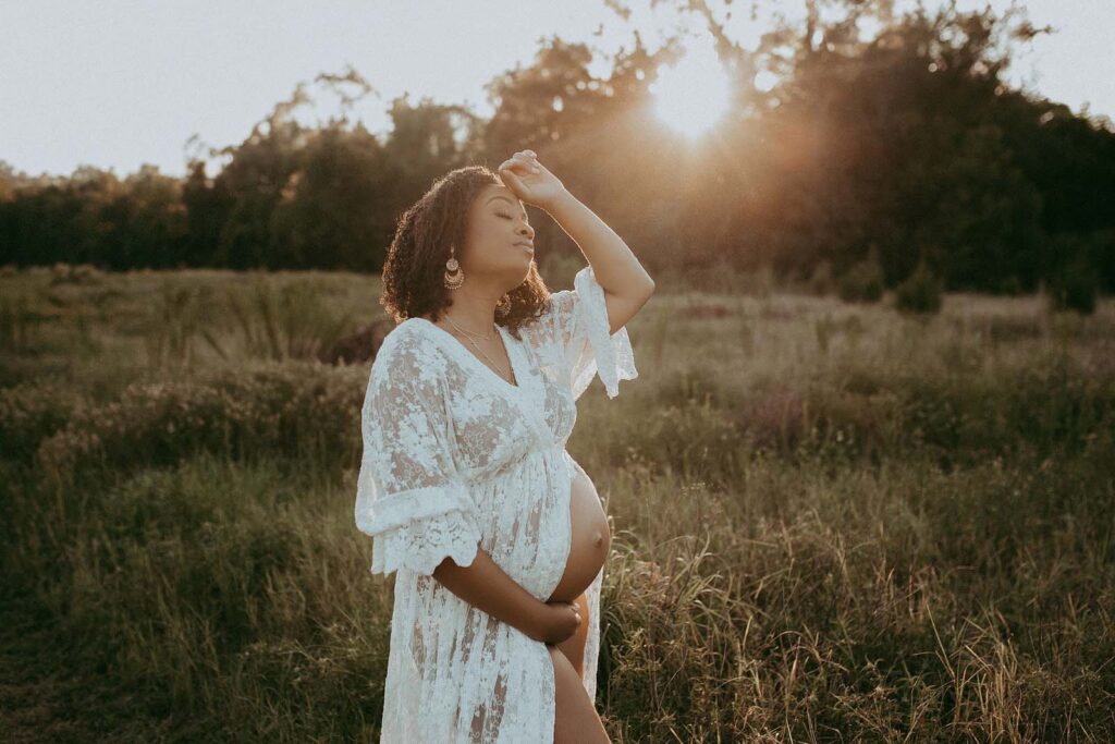 Beautiful mom-to-be is wearing white lace dress and posing to Durham maternity photographer near Baby Shower Venues Durham NC.