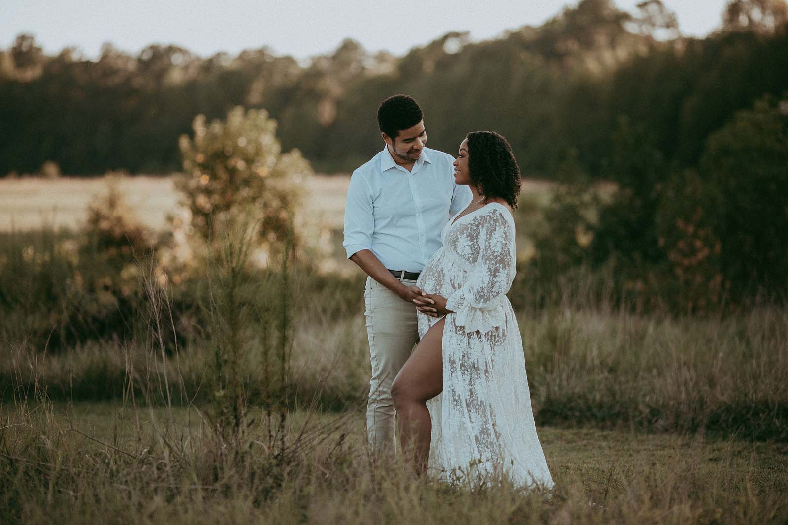 Dad-to-Be Embraces His Pregnant Wife in Maternity Photos. This photo shows a dad-to-be hugging his pregnant wife from her right side. They are both wearing white, and the photo is full of love and support. The photo is a beautiful reminder of the bond between a husband and wife, and the love they share for their unborn child. Maternity photographer - Victoria Vasilyeva Photography.