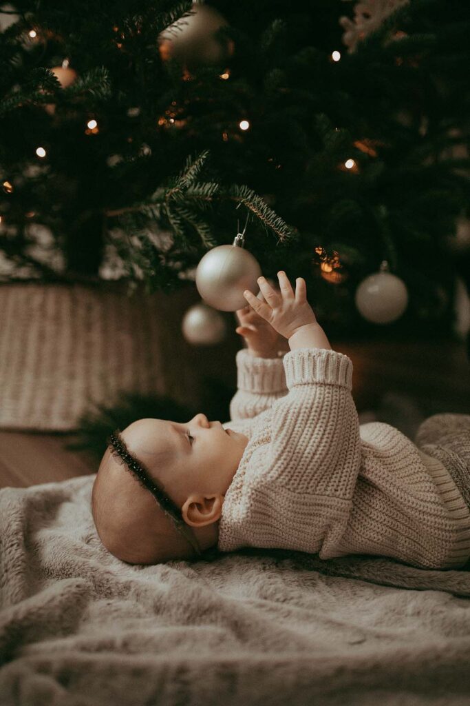 Adorable 5-month-old baby girl cuddling by the freshly cut Christmas tree in Raleigh, NC. Family Photo Session was made by Victoria Vasilyeva Photography.