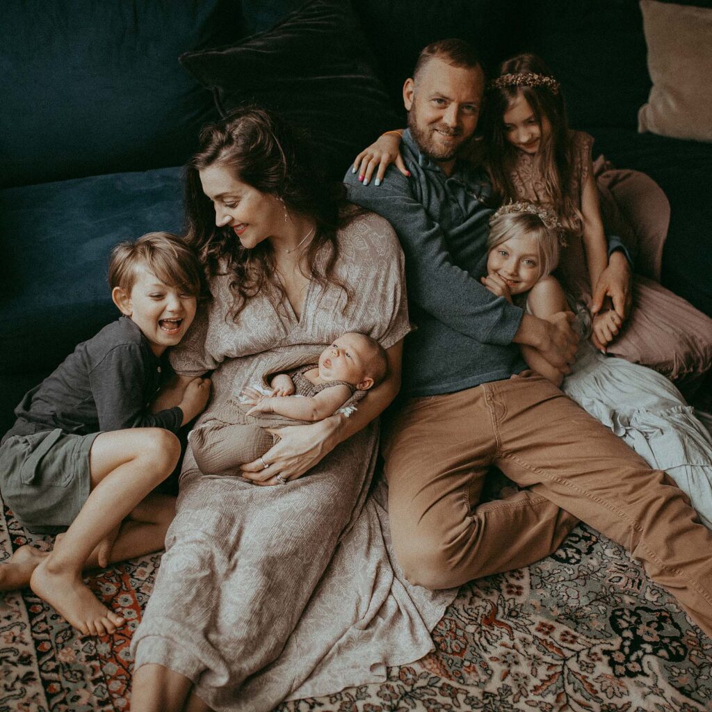 A loving family of six gathered in their cozy home, posing for a sweet portrait during a heartwarming in-home newborn photo session in Raleigh. Portrait by Victoria Vasilyeva Photography.
