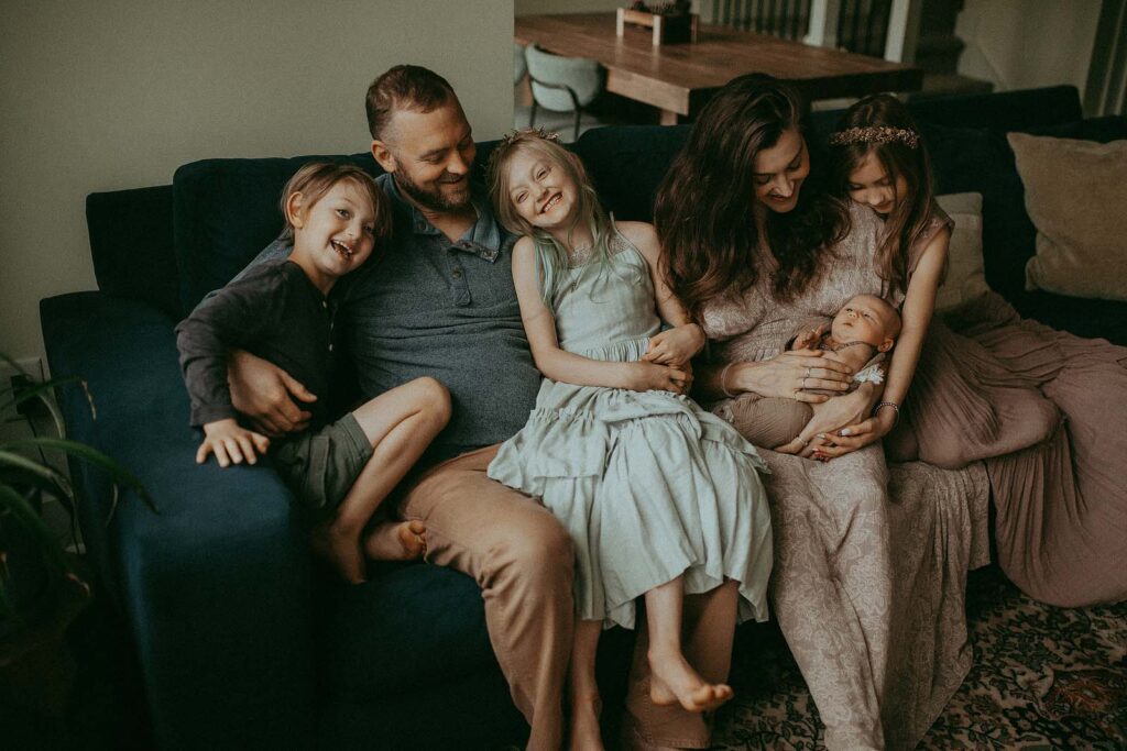 In the warm glow of their living room, a family of six smiles for the camera during a newborn photo shoot with Raleigh newborn photographer, showcasing the joy of welcoming their newest member.