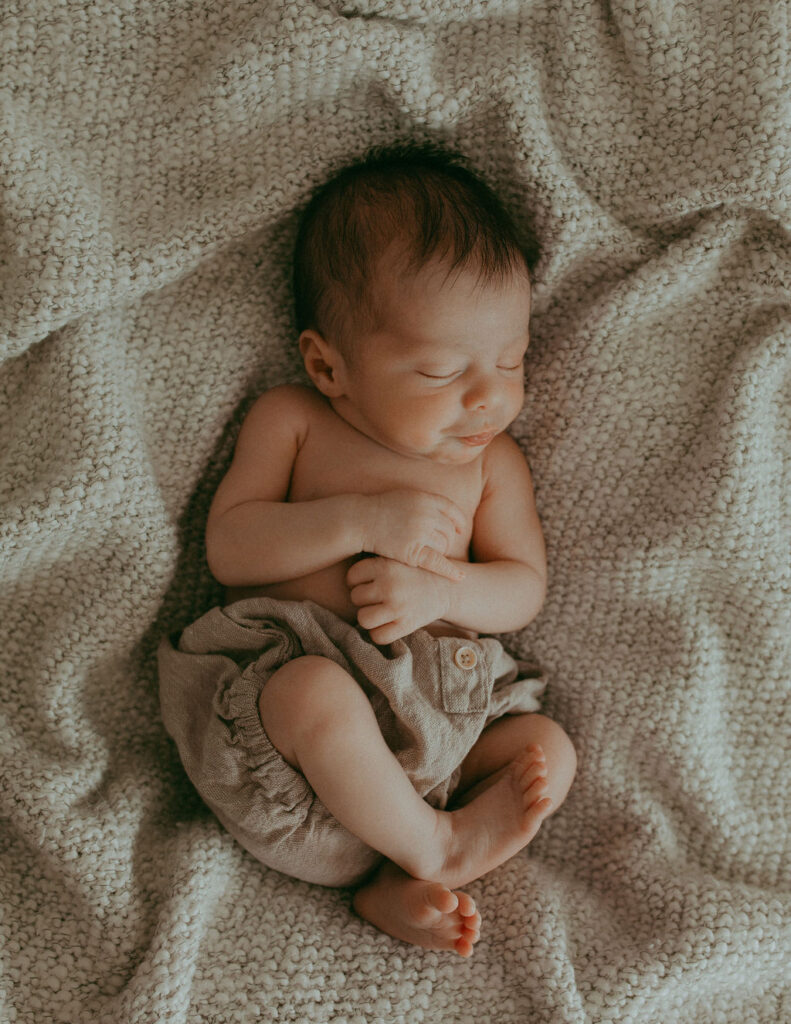 A newborn boy lays on a boho-themed blanket, exuding an irresistible charm.