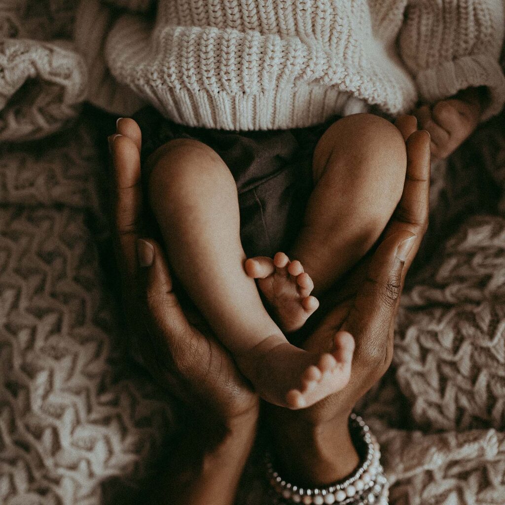 Newborn baby legs are hugged by mommy's arms. The photo was taken by Victoria Vasilyeva Photography - Greensboro newborn photographer.