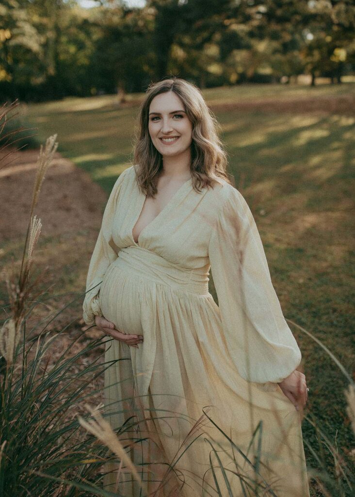 Capturing the beauty of maternity, a pregnant woman graces the scene in a maxi dress, radiating joy and positivity through her infectious smile. The portrait was taken after visiting Barefoot Babies ultrasound studio by Fayetteville maternity photographer - Victoria Vasilyeva Photography.