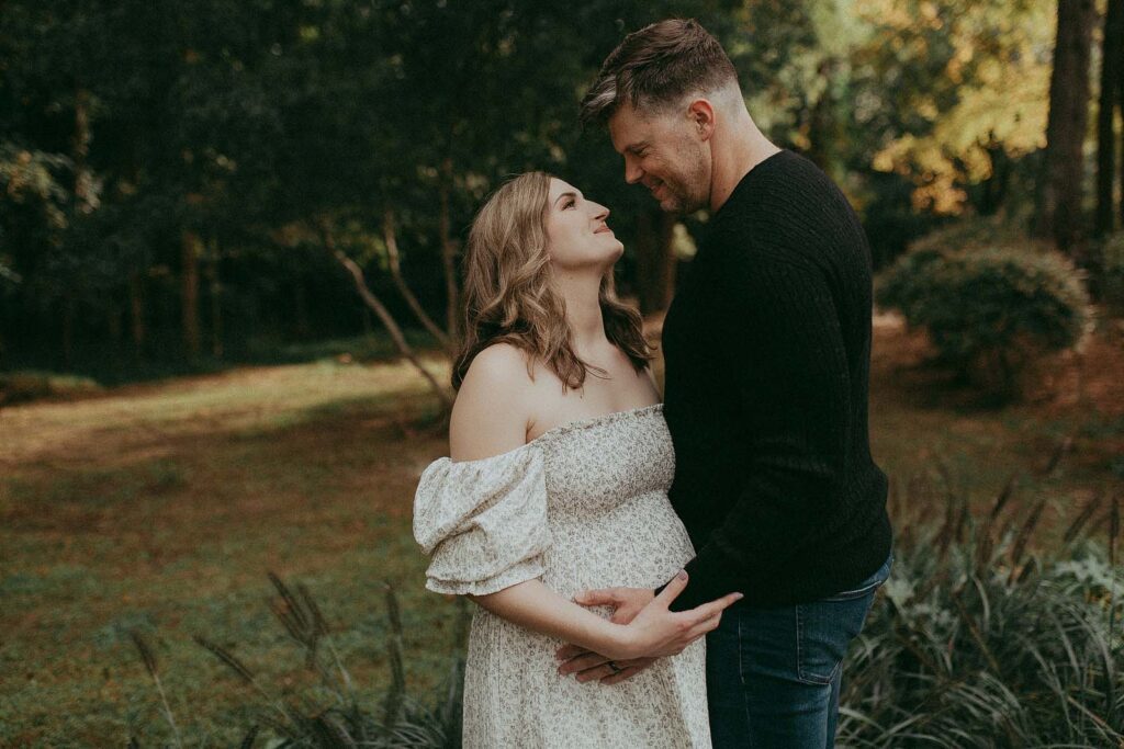 A snapshot of anticipation: A soon-to-be mom, elegant in a flowing maxi dress, and her partner, clad in a warm knitted sweater, share a serene moment of togetherness. Victoria Vasilyeva Photography - Fayetteville maternity photographer.