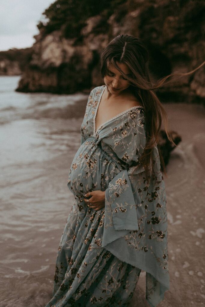 A beautiful expecting women in maxi blue dress is posing to Victoria Vasilyeva Photography - the award-winning Wilmington photographer, specializing in newborn, maternity, and family photographs.