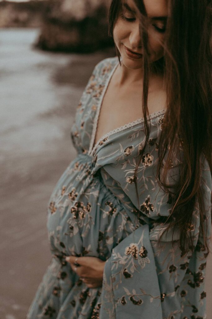 A beautiful expecting women in maxi blue dress is posing to Victoria Vasilyeva Photography - the award-winning Wilmington photographer, specializing in newborn, maternity, and family photographs.
