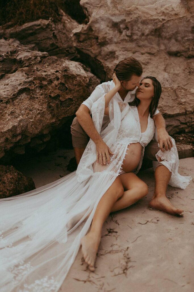 An expecting couple is posing on a beach during their maternity photo session. Victoria Vasilyeva Photography is one of the best maternity and family photographers in Wilmington, NC