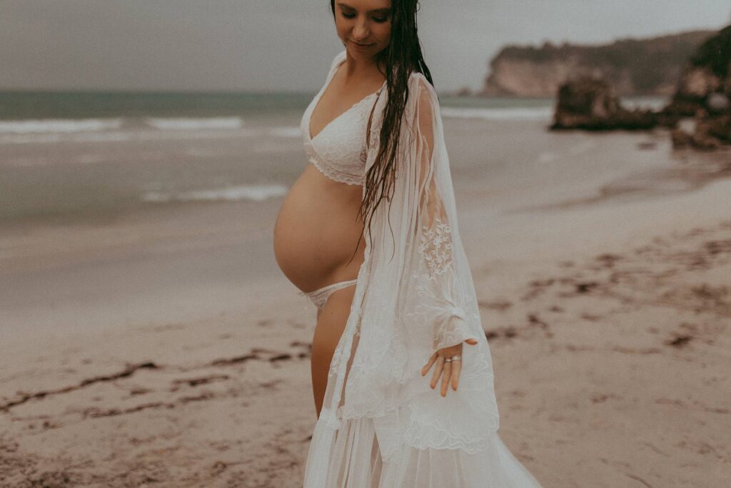 A beautiful pregnant woman in a white lace robe in boho style is posing to Victoria Vasilyeva Photography - one of the best maternity and family photographers in Wilmington, NC, and surrounding area.