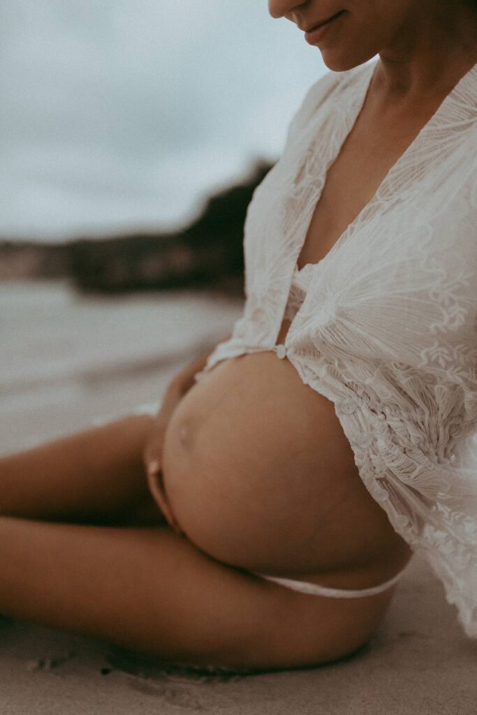 A beautiful pregnant woman in a white lace robe in boho style is posing to Victoria Vasilyeva Photography - one of the best maternity and family photographers in Wilmington, NC, and surrounding area.