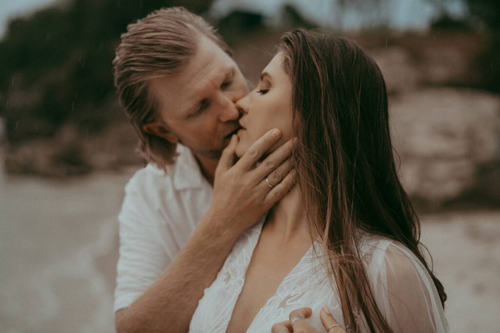 A beautiful expecting couple is sitting on the sand and posing to Victoria Vasilyeva Photography - one of the best maternity and family photographers in Wilmington, NC, and the surrounding area.