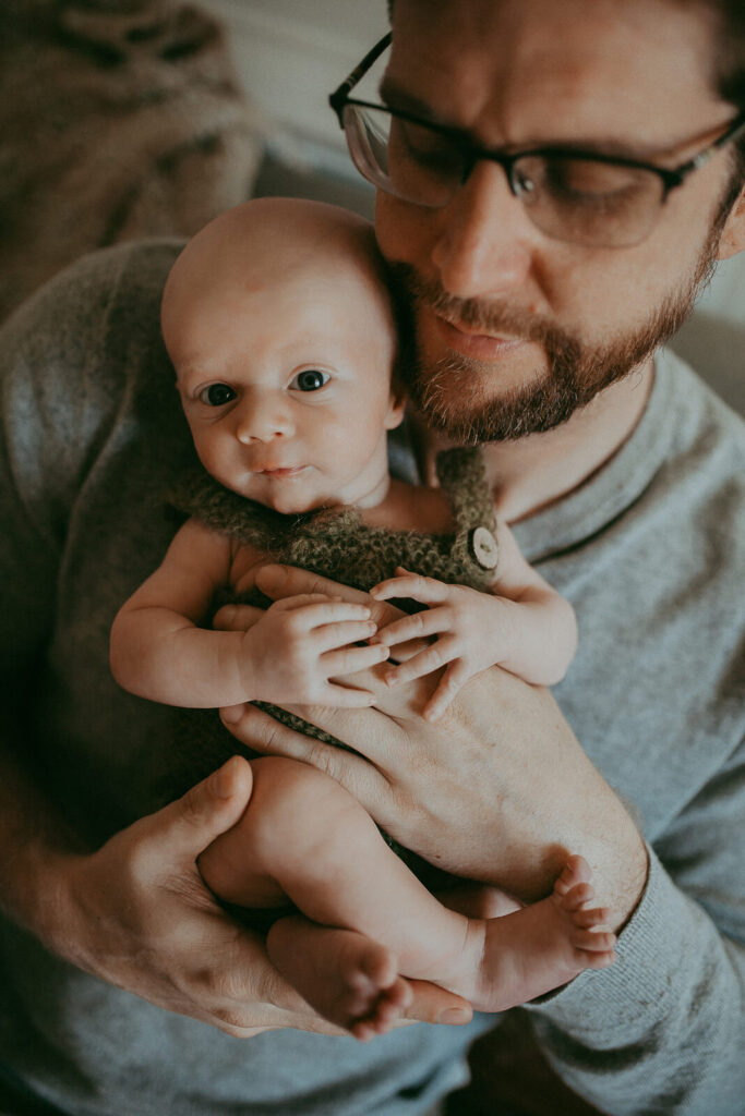 The portrait of newborn baby boy with his dad. Newborn photography in Cary, NC. Victoria Vasilyeva Photography specializes in lifestyle photography, using natural light. Certified, insured, professional, safety. All outfits for baby, mom, and siblings are provided.