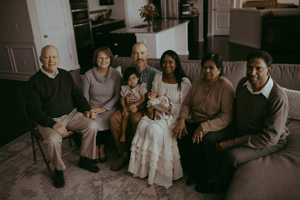 Big family with the 4-day-old baby boy is sitting on a couch in the living room. Victoria Vasilyeva Photography - Certified, insured, and professional baby photographer in Greensboro. All outfits for baby, mom, and siblings are provided. Newborn Photography Greensboro NC