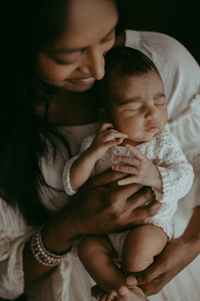 Newborn photo session with 4-days-old baby boy and his family. The portrait of mom and baby in white romper was taken by Victoria Vasilyeva Photography - Certified, insured, and professional Greensboro photographer.