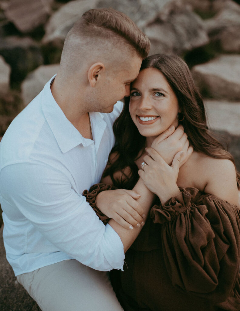 A romantic sunset shot of the mom-to-be, in a brown maxi dress, sitting beside her husband at NCMA, her hand gently resting on his hand.