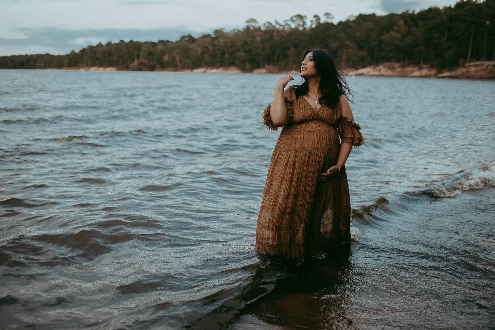 Maternity session at the lake, featuring a glowing mom in a boho maxi dress, wind gently lifting the fabric and her long black hair.