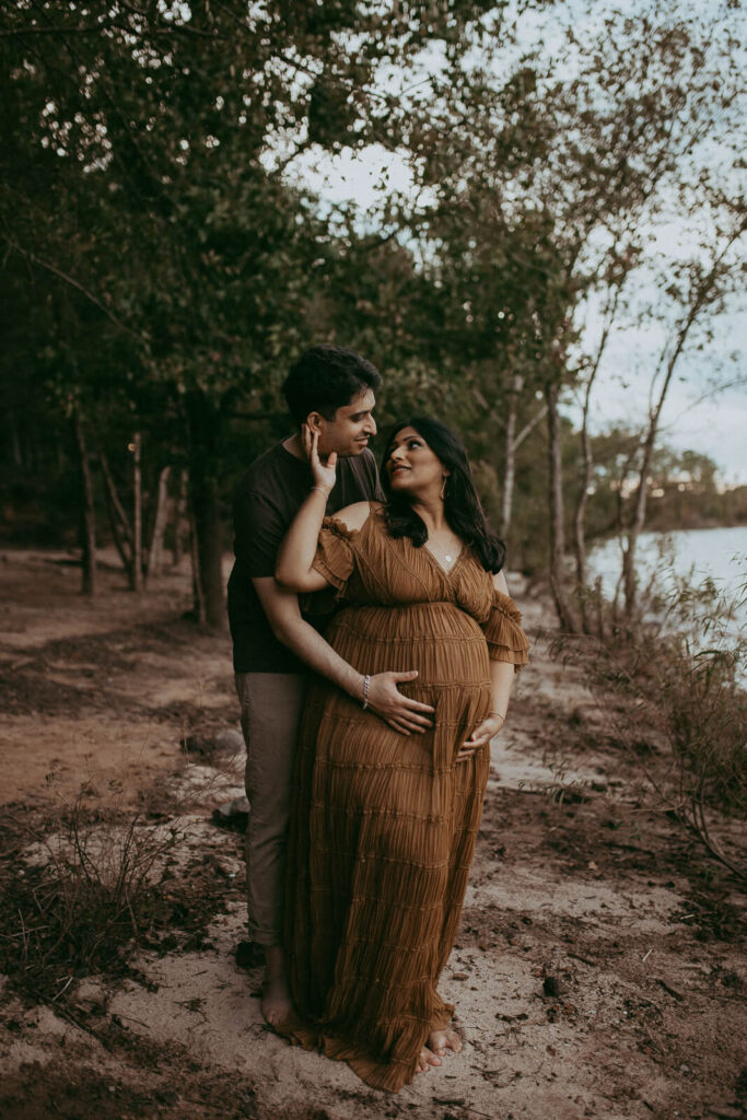 Lakeside maternity portrait with an expecting couple laughing together, enjoying the peaceful setting.