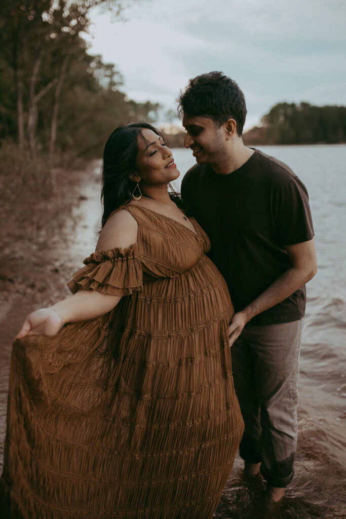 Maternity couple embracing by the lake at a serene Fayetteville location, photographed by Victoria Vaslyeva Photography.