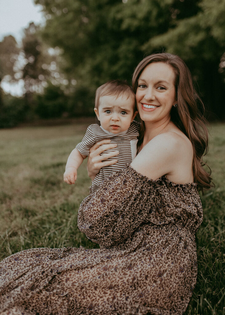 A mother and cute baby boy smile at camera. A mother has long wavy hair.
