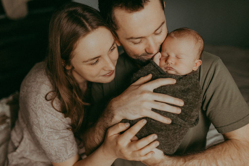 This close-up, overhead photo features a peacefully sleeping newborn baby with parents, cozy in a textured green blanket, a common scene related to the support provided by Lactation Consultants in Fayetteville, NC
