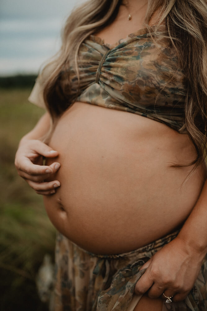 Close-up maternity photo of a woman’s pregnant belly in a floral two-piece gown during an outdoor session. Used in an article discussing 4D Ultrasound Raleigh NC.