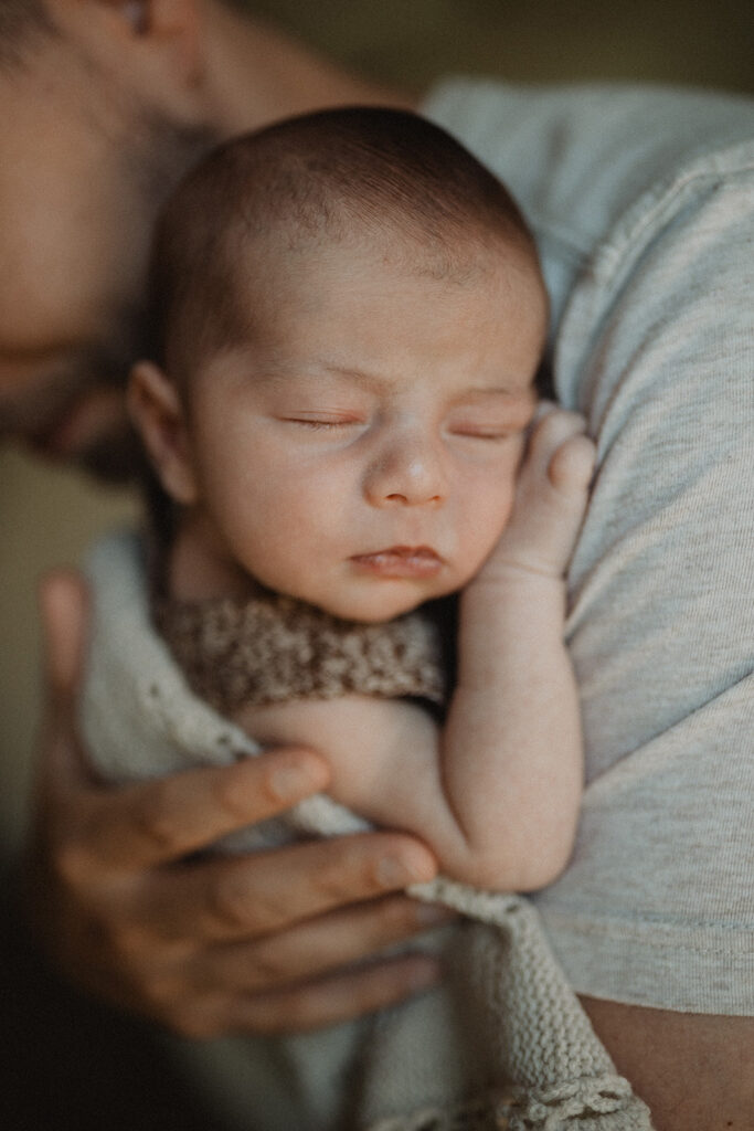 Close-up portrait of a sleeping newborn resting on a parent’s shoulder, a serene lifestyle image reflecting early infancy and routines before infant swim lessons Durham NC begin.