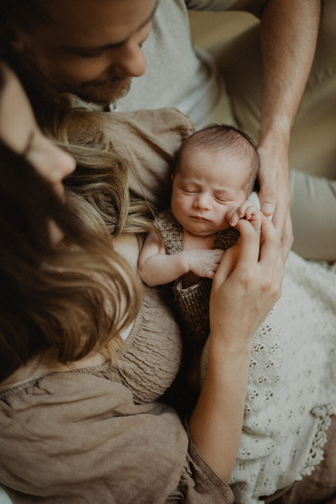 Parents cradling their newborn together on a bed, hands gently supporting the baby, representing nurturing care and safety important for families considering infant swim lessons Durham NC.