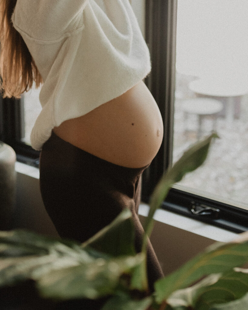 Close-up of a pregnant belly near a window, symbolizing body awareness, relaxation, and prenatal massage benefits at Moonshadow Medical Massage.